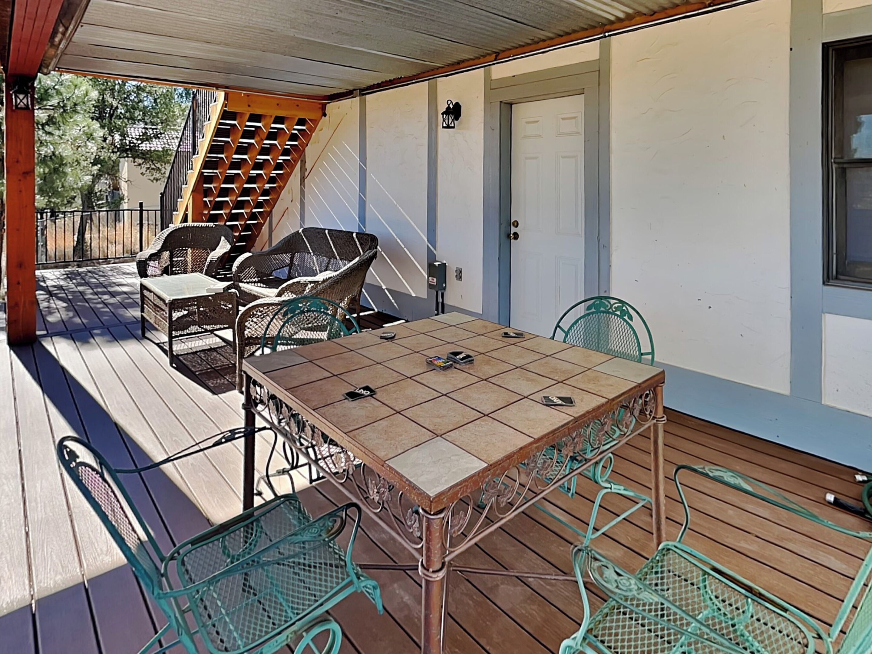 A covered patio with a table and chairs, a wooden deck, and a white door.