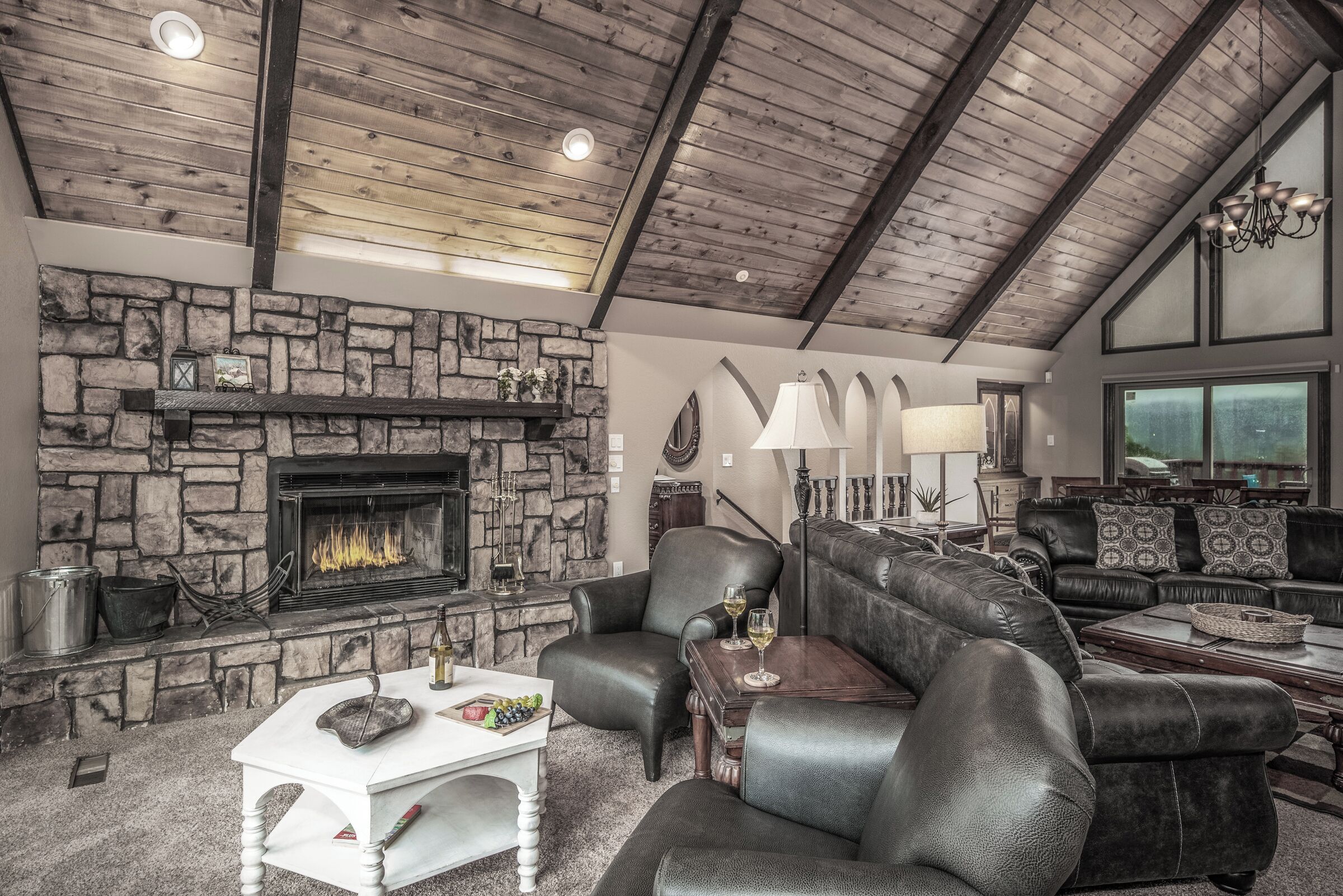 A cozy living room with a stone fireplace, leather sofas, and a high wooden ceiling.