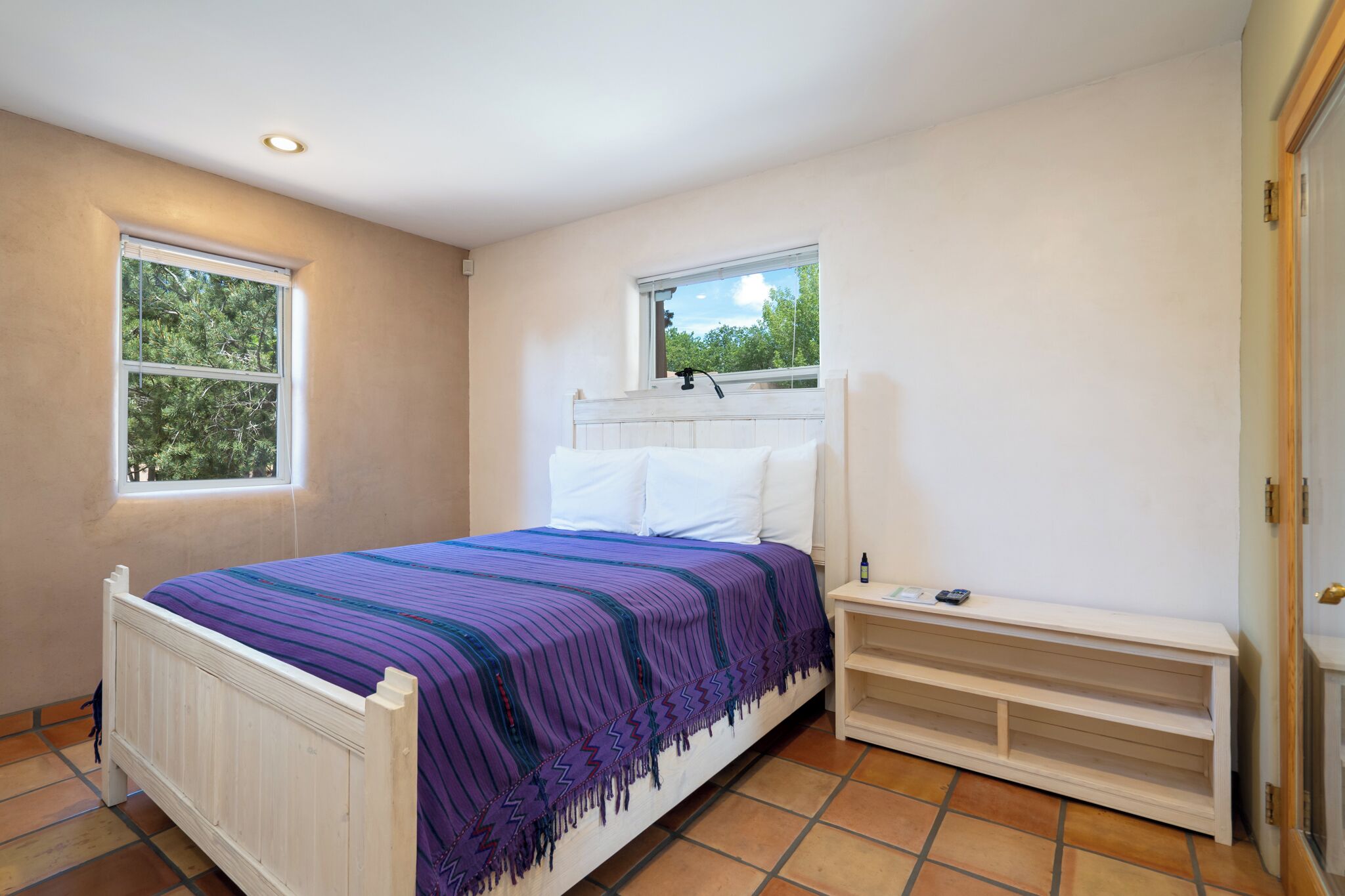 A bedroom with a bed, two windows, a bedside table, and a built-in bench.