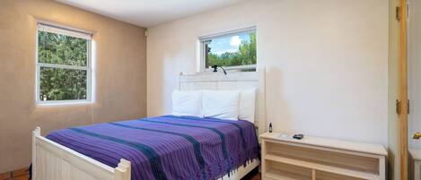 A bedroom with a bed, two windows, a bedside table, and a built-in bench.