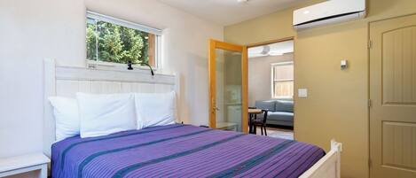 A bedroom with a bed, a window, an air conditioning unit, and a door.