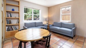 A living room with a wooden table, two sofas, a bookshelf, and large windows. - Casa Columbia by Kokopelli Property Management (Santa Fe)