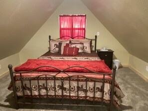 A bedroom with a bed, a nightstand, a window with curtains, and a carpeted floor. - Cowboy Cabin is nestled in a little woodland village – playground, pond and more (Winslow)