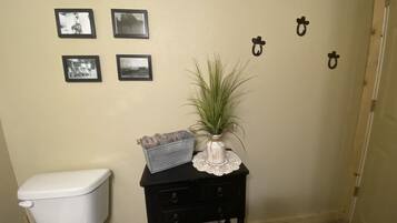 A bathroom with a toilet, a small table with a plant and a towel, and three framed pictures on the wall.