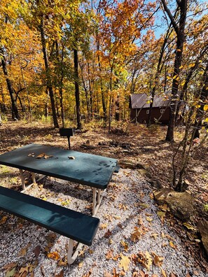 A picnic table and bench in a forested area with a cabin in the background. - Cowboy Cabin is nestled in a little woodland village – playground, pond and more (Winslow)