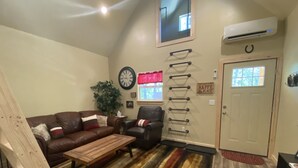 Una sala de estar acogedora con un sofá de cuero marrón, una mesa de centro de madera, un sillón negro, un tapete a rayas, un reloj grande, una planta en maceta y una puerta con ventanal.