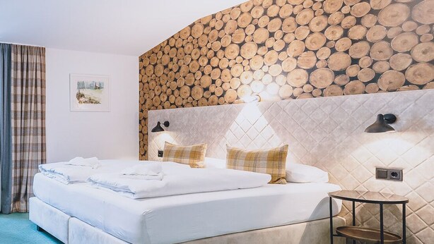 A bedroom with a large bed, a bedside table, and a wall covered with logs. - Alpine City Living - TOP 33, City center & modern (Zell am See)