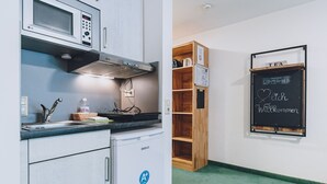 A kitchenette with a microwave, stove, and sink. There's a chalkboard with a welcome message and a shelf with a kettle. - Alpine City Living - TOP 33, City center & modern (Zell am See)
