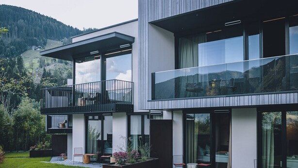 Et moderne hus med to etager, en balkon, store vinduer og en velplejet have.