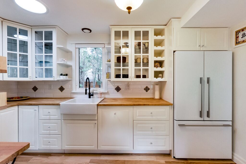 A kitchen with white cabinets, a wooden countertop, a sink, and a refrigerator.