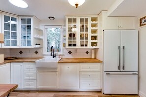 A kitchen with white cabinets, a wooden countertop, a sink, and a refrigerator. - Niagara Wine Country Cottage (Lincoln)