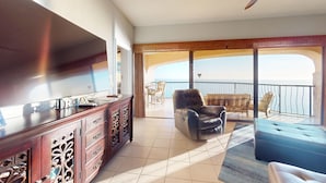 Ein Zimmer mit Fernseher, Holzschrank, Ledersessel, einer Couch und einem Balkon mit Meerblick.