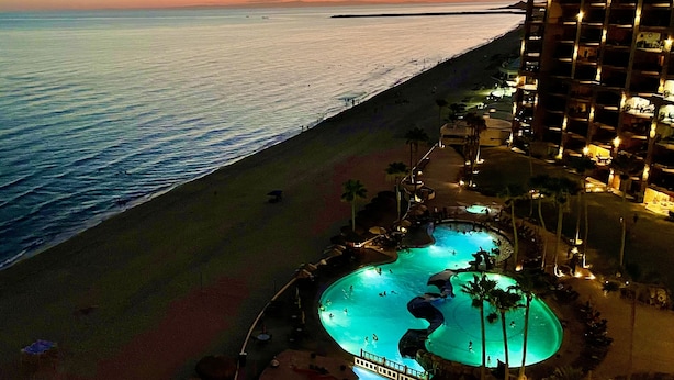 Ein Resort mit großzügigem Poolbereich, einem Strand und Blick auf den Sonnenuntergang über dem Meer.