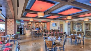 Ein Restaurant mit modernem Interieur, das eine Mischung aus Holz- und Metallmöbeln, einen Barbereich und eine Sitzordnung mit Tischen und Stühlen zeigt.