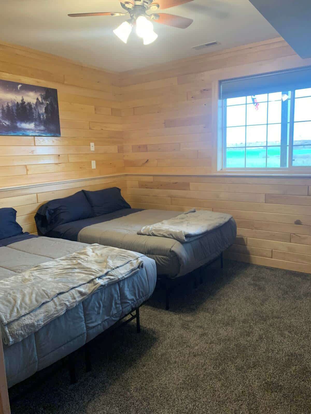 Une pièce aux murs en bois, avec deux lits, un ventilateur de plafond et une fenêtre donnant sur un beau paysage.