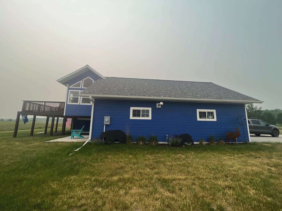 A single-story house with a blue exterior, a covered porch, and a grassy yard.