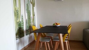 Ein Essbereich mit einem schwarzen Tisch und gelben Stühlen, einer Obstschale auf dem Tisch und einer Wandmalerei mit Kakteen.