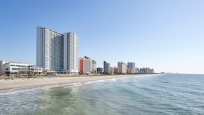 A beachfront hotel with multiple high-rise buildings, a sandy beach, and a clear blue sky.
