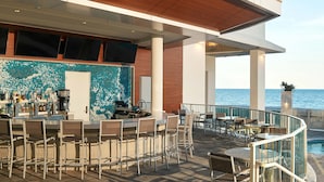 A bar area with chairs and tables, a pool, and a view of the sea.