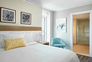 A hotel room with a bed, a nightstand, a lamp, a chair, and a shower area. - Myrtle Beach SC | Partial Ocean View Seaside Getaway | Pool + Beach (Myrtle Beach)