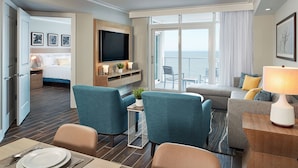A hotel room with a bed, a TV, a seating area with chairs, a sofa, and a balcony with a view.