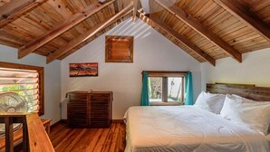 Ein Schlafzimmer mit Holzbalken, einem Bett, einem Fenster mit Vorhängen und einem Ventilator.