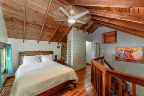 A bedroom with a wooden ceiling, a bed, a staircase, and a painting on the wall.