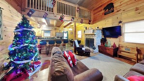 A cozy cabin interior with a decorated Christmas tree, a fireplace, a kitchen area, and a bar. - Mountain Dreams by Jackson Mountain Rentals (Gatlinburg)