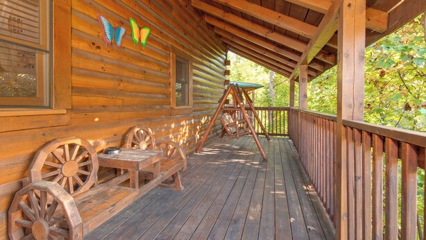A wooden cabin with a porch, wooden benches, and a swing set. - Mountain Dreams by Jackson Mountain Rentals (Gatlinburg)