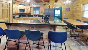 A wooden cabin interior with a kitchen area, a dining table with chairs, and a large island. - Mountain Dreams by Jackson Mountain Rentals (Gatlinburg)