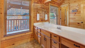 Baño de cabaña de madera con un lavamanos grande, armarios de madera y una ventana con persianas.