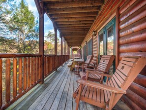 A wooden deck with a covered porch, wooden chairs, and a table.