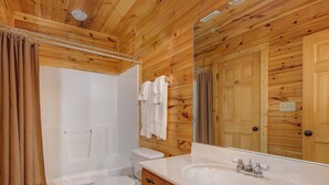 Un baño con paneles de madera, una bañera, un inodoro y un espejo grande.
