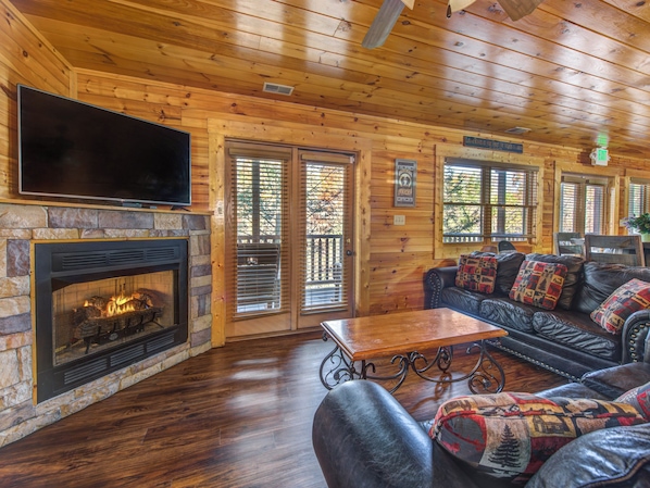 A cozy cabin interior with a stone fireplace, leather sofa, and a flat-screen TV mounted above it.