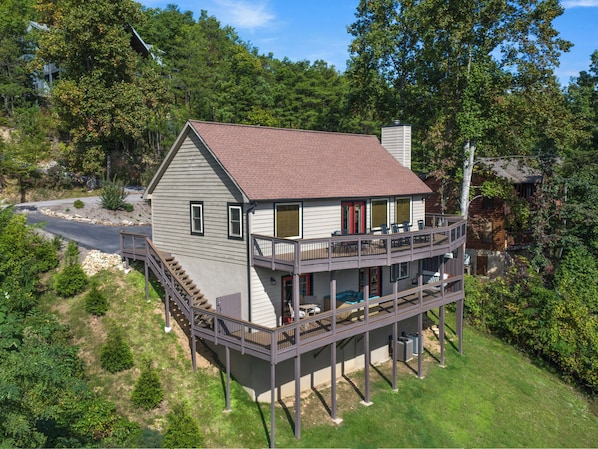 A two-story house with a balcony, surrounded by trees and a road.