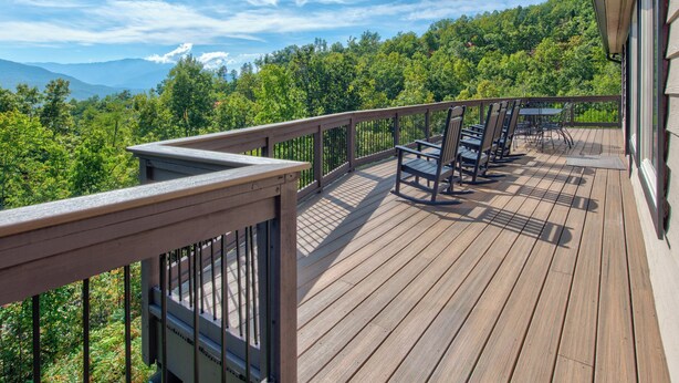 A wooden deck with a railing, outdoor seating, and a view of a forest and mountains. - On Eagle's Wings by Jackson Mountain Rentals (Gatlinburg)