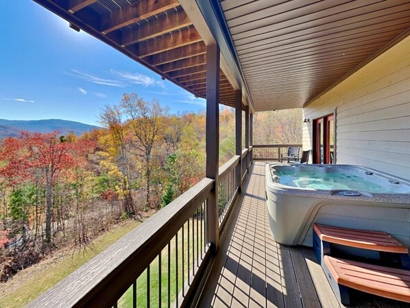 A wooden deck with a hot tub and benches, overlooking a forest with autumn foliage. - On Eagle's Wings by Jackson Mountain Rentals (Gatlinburg)