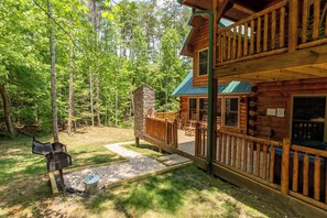 A cabin with a deck, stone chimney, and outdoor seating area surrounded by trees. - Fire in the Sky by Smoky Cove Resort (Sevierville)