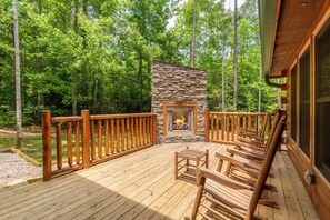 A wooden deck with a stone fireplace, surrounded by a wooden railing, set in a forested area. - Fire in the Sky by Smoky Cove Resort (Sevierville)