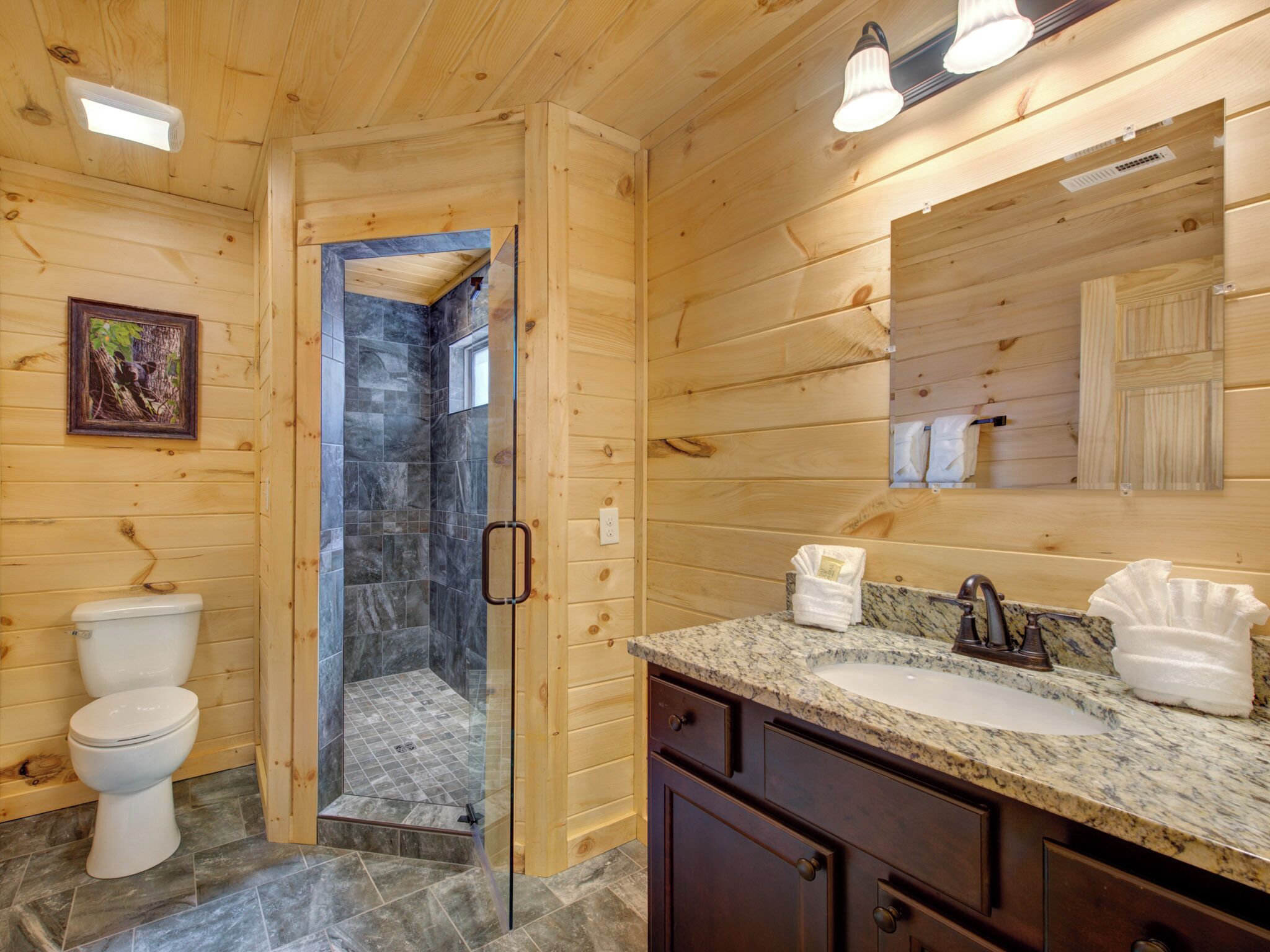 Une salle de bain rustique, avec une cabine en bois, une douche en verre, un lavabo doté d’un plan de travail en marbre et un miroir au-dessus du lavabo.