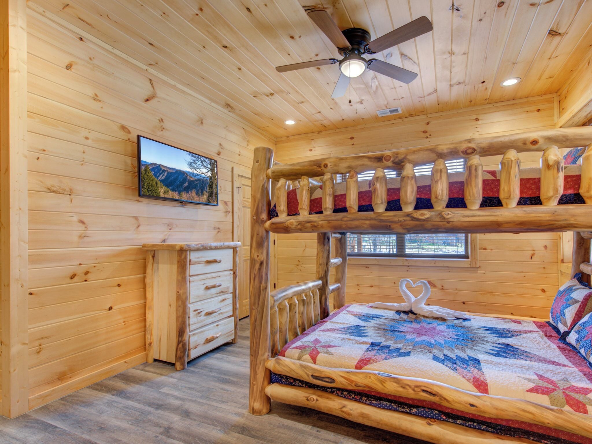 Une chambre dans une cabane en bois, avec un lit superposé, un ventilateur de plafond, une commode et une fenêtre donnant sur la montagne.