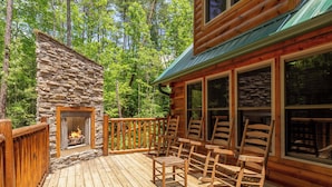 Une terrasse en bois avec une cheminée en pierre, des chaises en bois et une structure de type cabane en rondins.