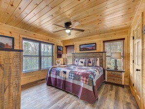 A wooden cabin bedroom with a bed, a ceiling fan, and large windows.