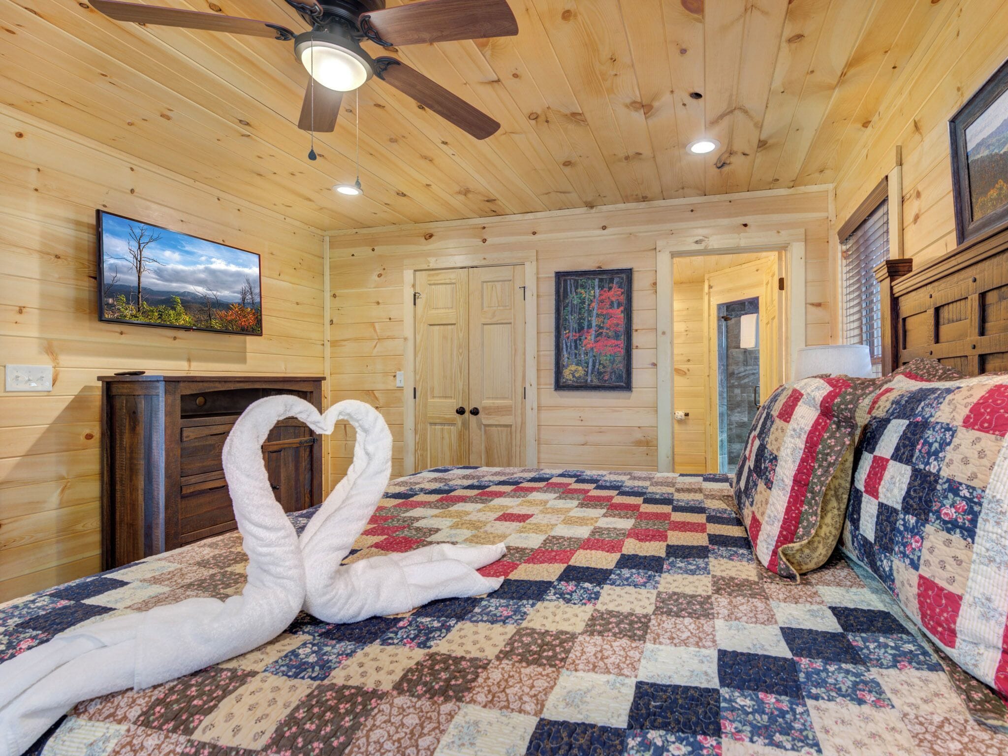 A cozy room with a wooden ceiling, a bed with a quilt, a fireplace, and a painting on the wall.