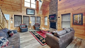 L’intérieur d’une cabane en rondins, avec une cheminée, des murs en bois et un ventilateur de plafond.