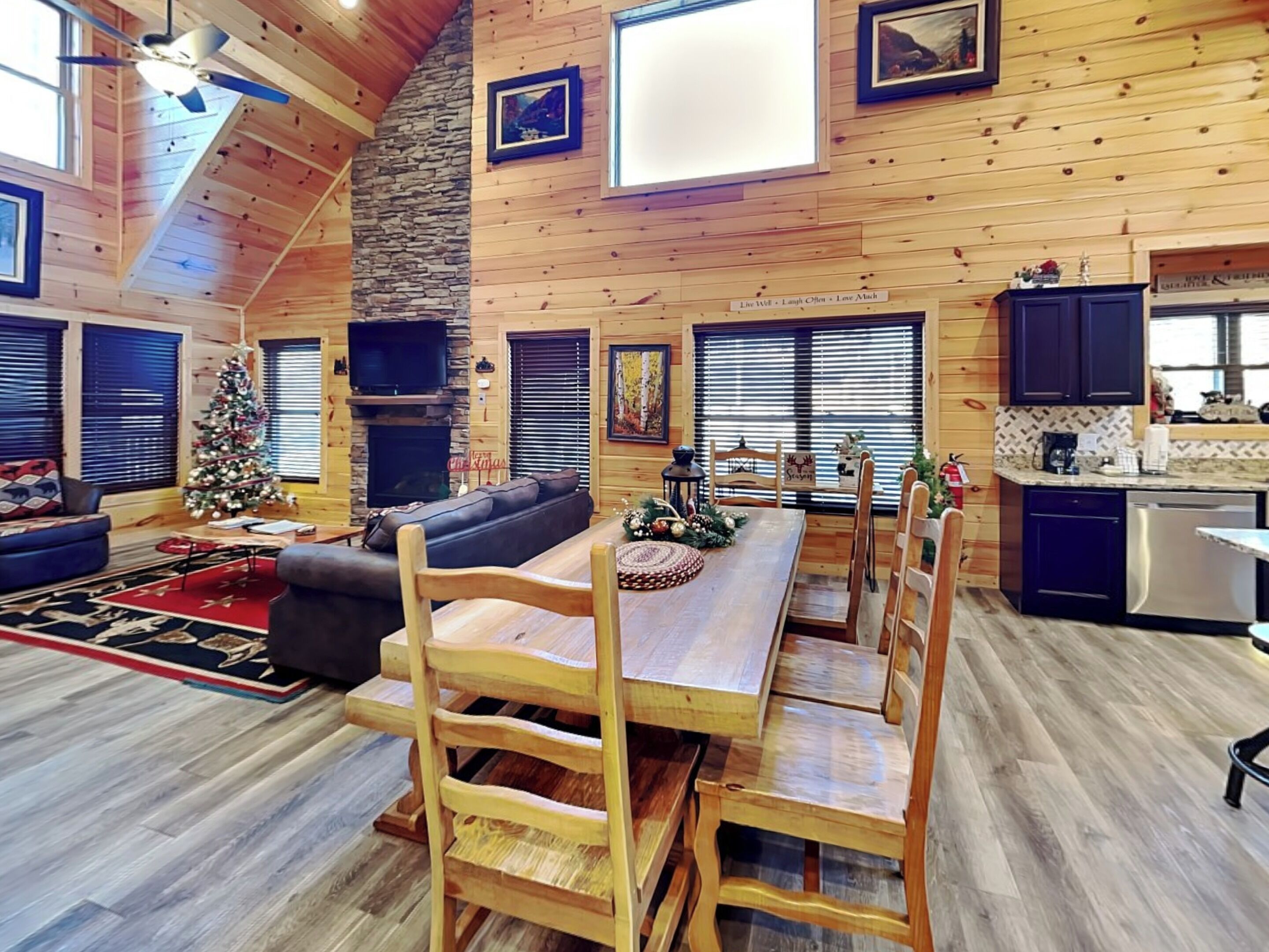 A spacious living room with a fireplace, a dining area with wooden chairs, a Christmas tree, and a kitchen area with dark cabinets.