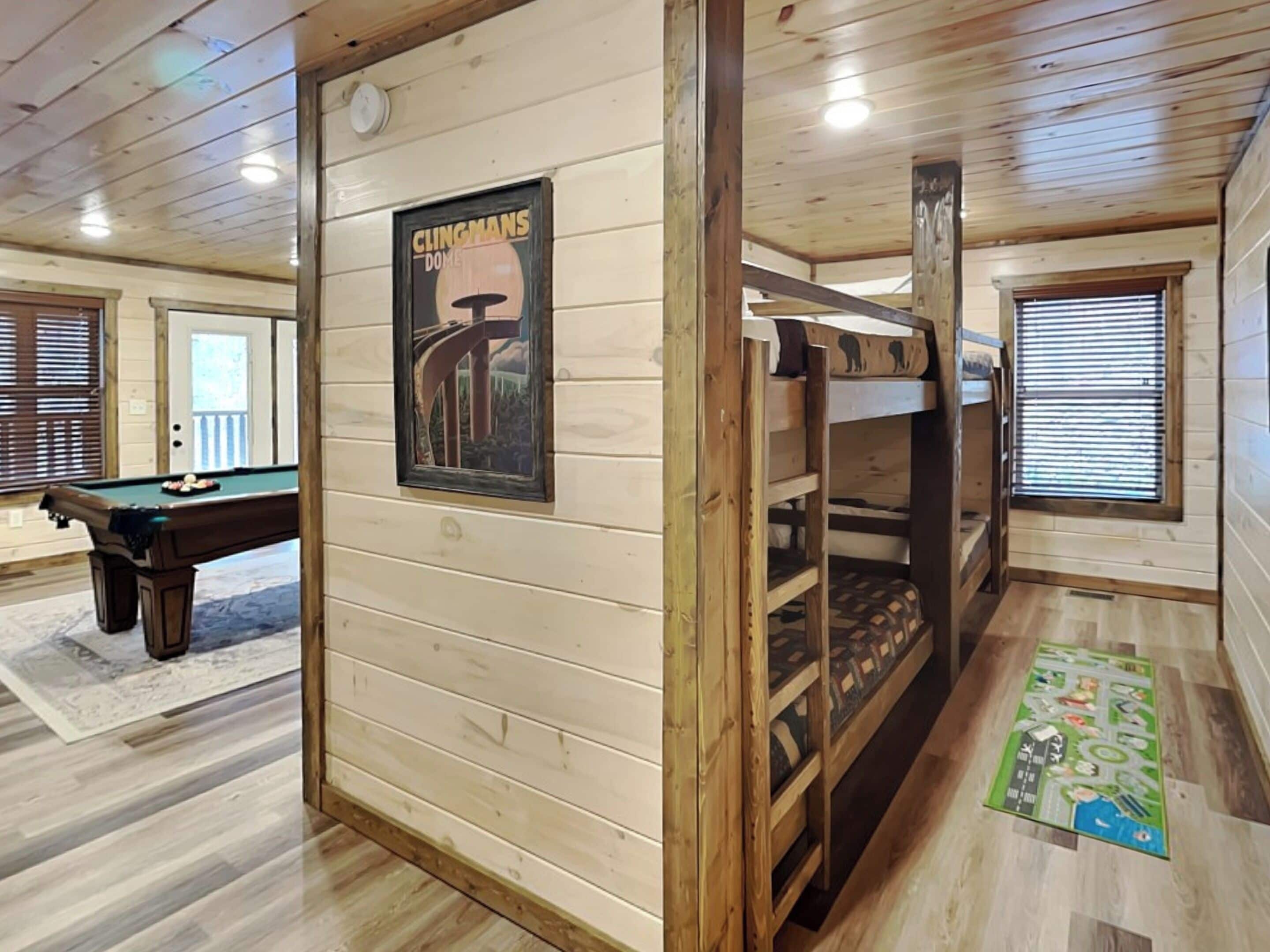 Ein Holzblockhaus-Interieur mit Stockbetten, einem Billardtisch und einem Poster einer Brücke.