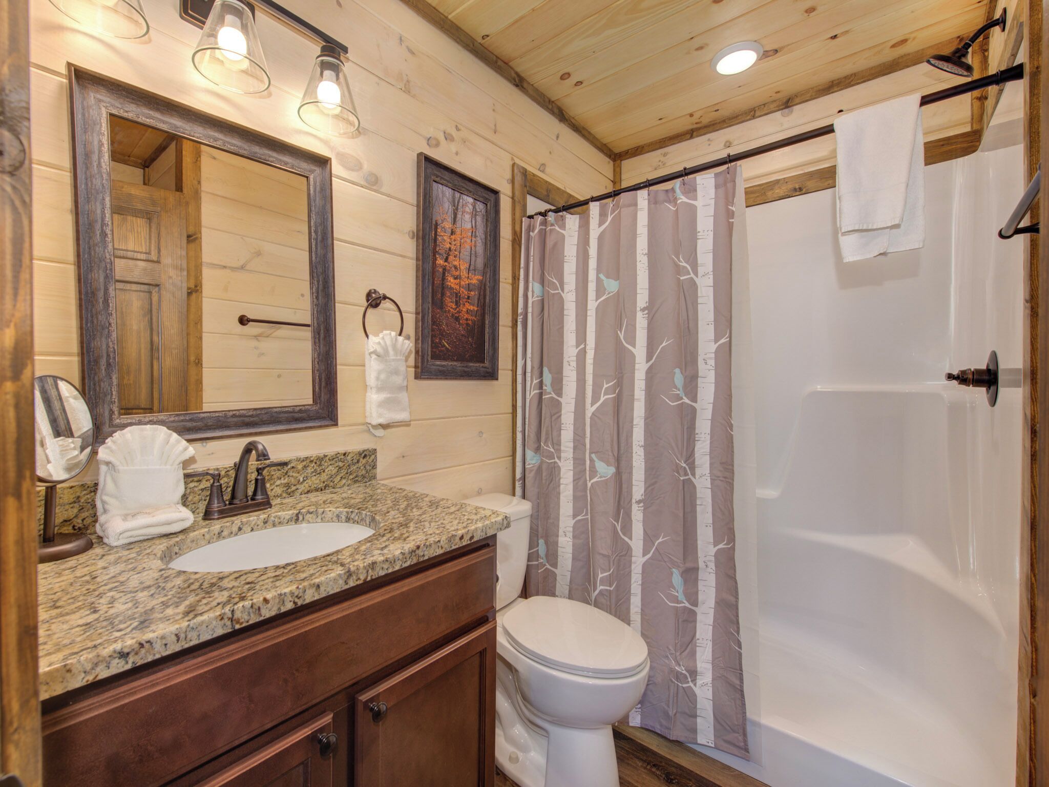 A wooden cabin bathroom with a granite sink, a toilet, and a shower with a tree-patterned curtain.