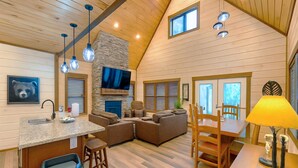 A spacious living area with a stone fireplace, a television mounted on the wall, and a dining area with wooden furniture. - Twisted Pines by Smoky Cove Resort (Sevierville)