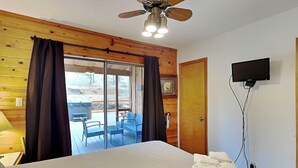 A bedroom with a large bed, a ceiling fan, a television, and a sliding glass door leading to an outdoor area with chairs. - Moose Manor by Ruidoso Vacation Rentals (Ruidoso)